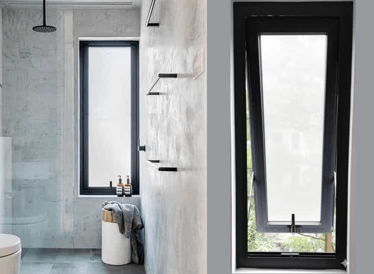 Sleek black aluminium awning window with frosted glass providing essential privacy and ventilation in a modern bathroom with grey concrete-look walls and a glass shower enclosure.