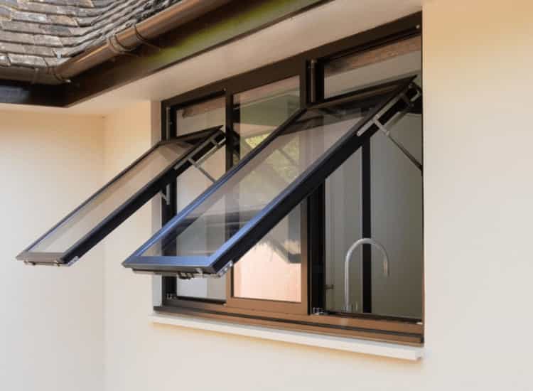 High-quality black aluminium awning windows installed on a white kitchen exterior wall. The two upper sashes are cranked open from the bottom, while the middle sash is fixed and views the kitchen sink.