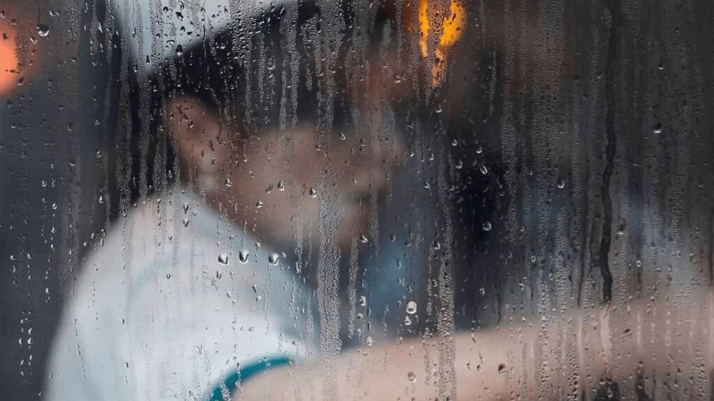 Close-up of heavy water droplets and condensation covering a glass window pane, illustrating excessive indoor humidity buildup.