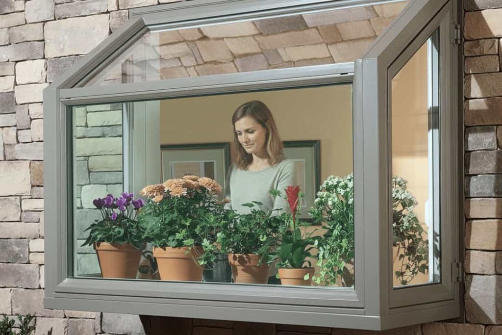 A sleek, modern aluminium garden window in a kitchen, providing a shelf for growing fresh herbs and small potted plants under maximum sunlight.
