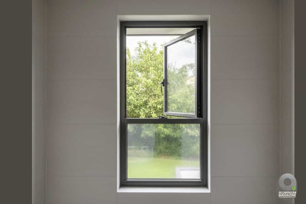 Single-panel aluminium casement window, partially open, with a fixed lower panel looking out to a garden.