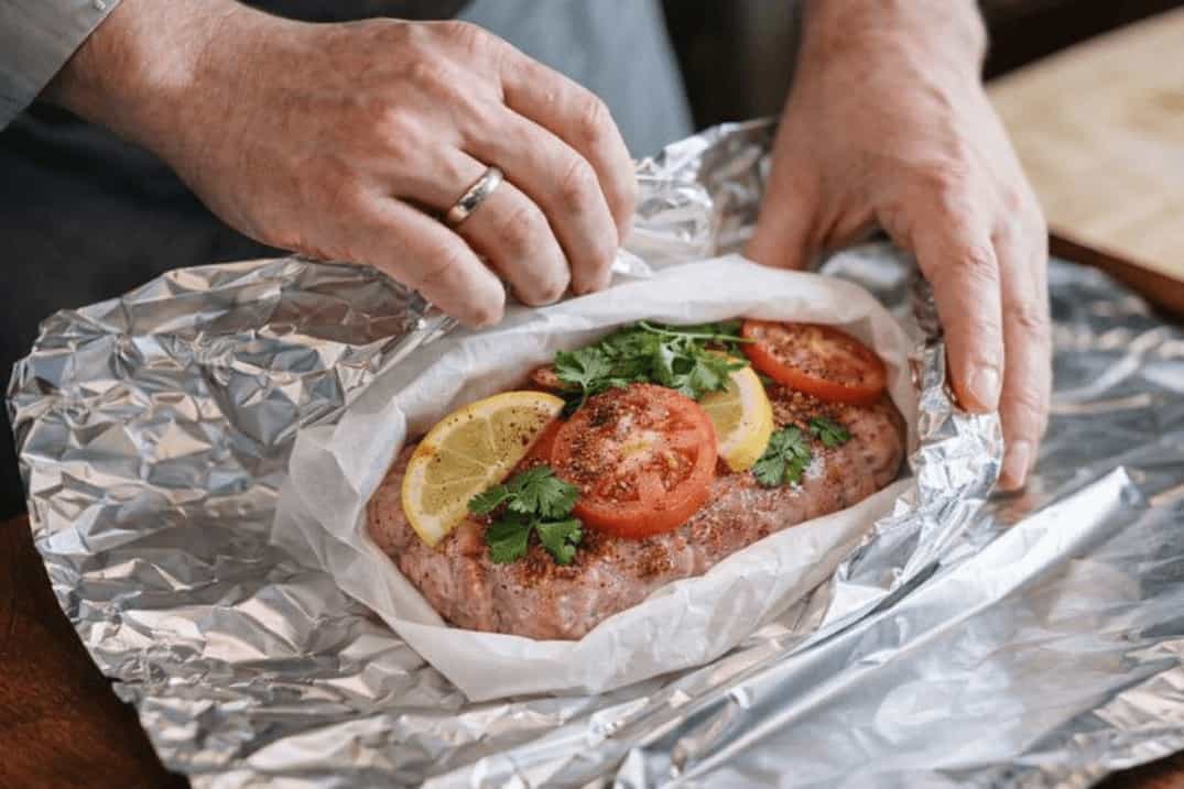 Meat wrapped in parchment paper and aluminium foil with tomato lemon and herbs for cooking