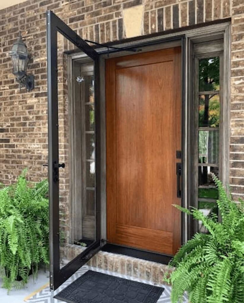 A sleek black aluminum storm door with a full-view glass panel installed over a wooden front door on a brick house.