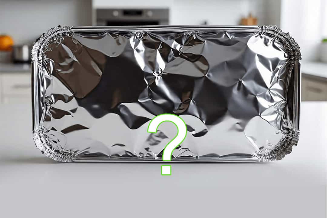 Unrolled sheet of aluminum foil on a dark counter with a subtle question mark imprint, representing common kitchen myths.