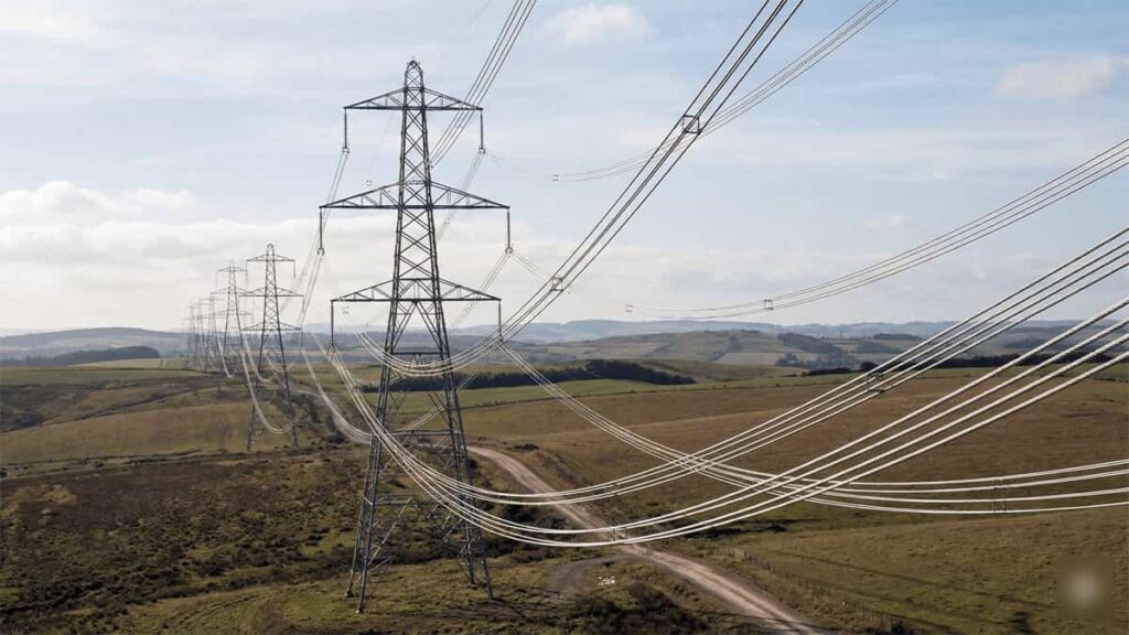 High-voltage overhead power transmission lines supported by steel pylons extending across a rural landscape.
