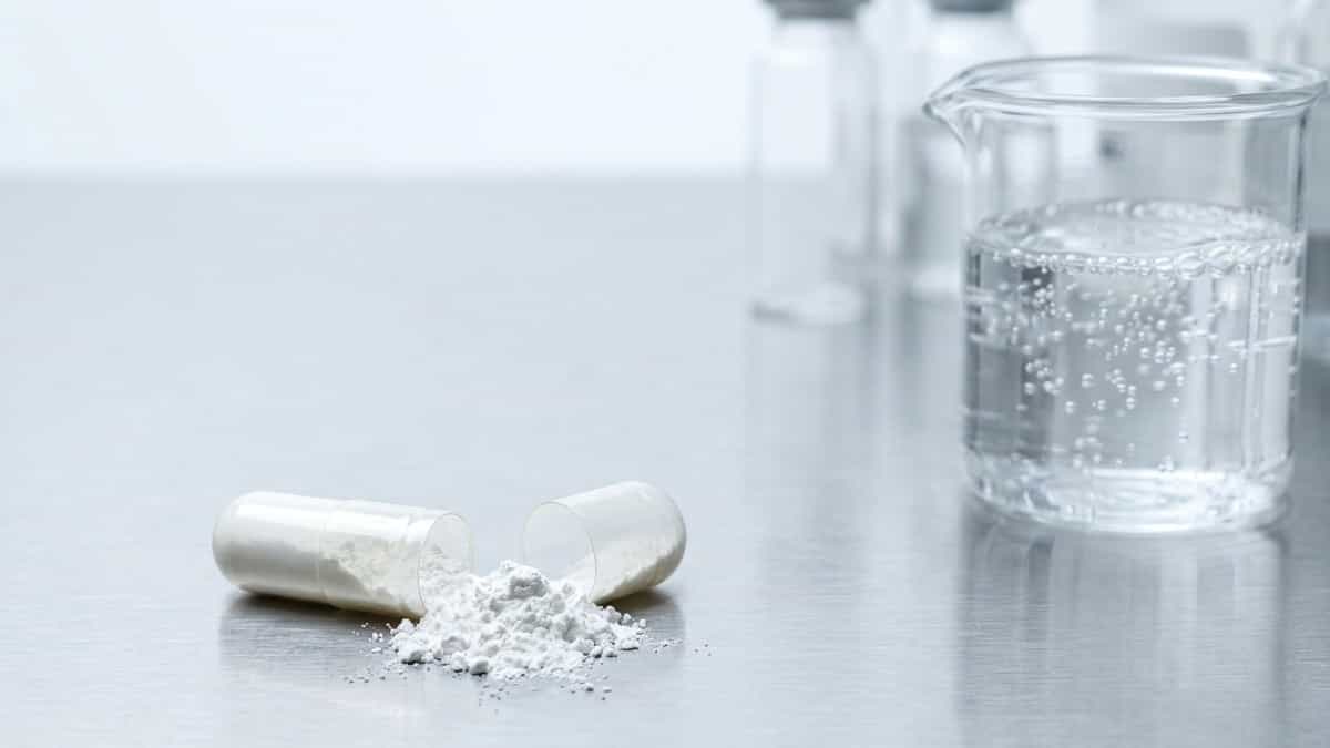 High-resolution photograph of white basic aluminum carbonate powder spilling from a pharmaceutical capsule on a clean surface.