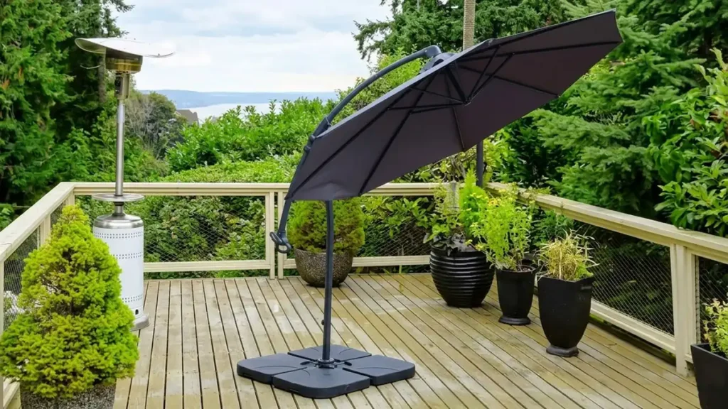Dark grey cantilever aluminium umbrella with heavy-duty base set up on a wooden patio deck overlooking a scenic view.