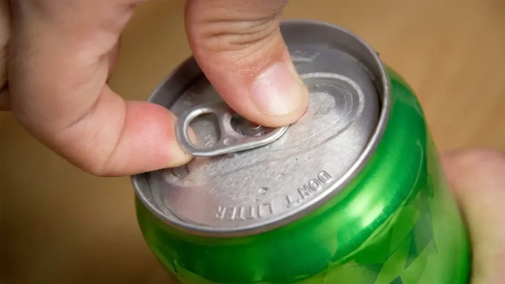 A hand lifting the stay-on tab of a cold aluminium soda can, showing the modern ecology tab design.